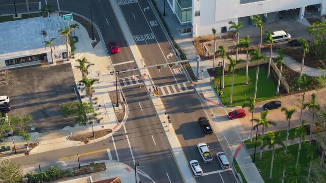 Dynamic street scene in Sarasota with people walking across a pedestrian crossing while traffic lights control the flow of vehicles at a busy junction.