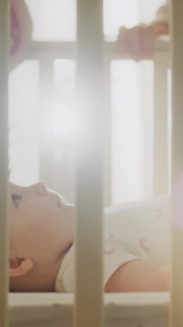 Young mother rocks newborn baby in crib on sunny day, soft sunlight streams through window, gently swaying the wooden cradle until the infant closes its eyes and rests, a typical infant sleep routine