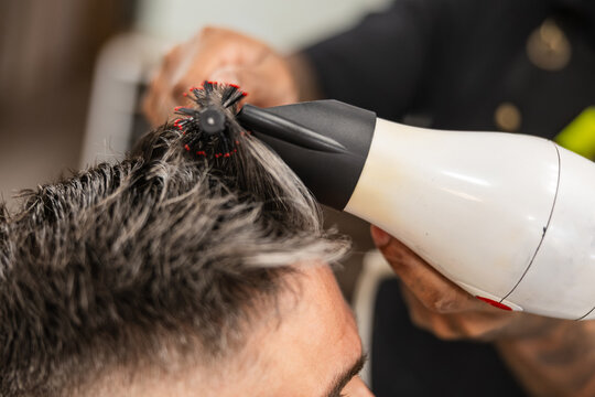 Barber styling man's hair with blow dryer