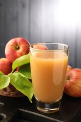 Fototapeta premium Apple juice in glass, fresh fruits and leaves on black table, closeup