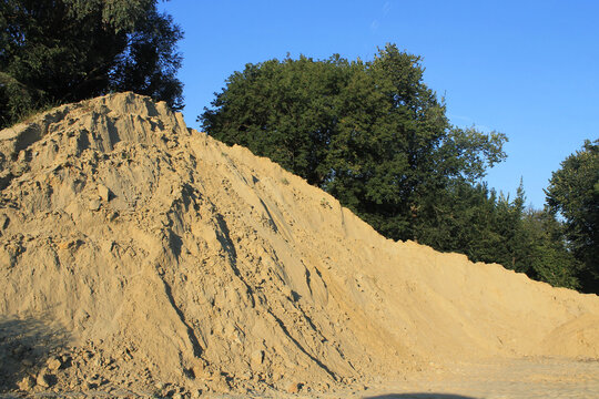 Construction sand. A mountain of sand lies on a next to road. Materials for creating an embankment.
