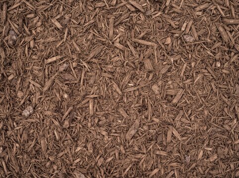 A close-up, high-angle view of brown wood chips or garden mulch covering a surface, showing various textures and shades.