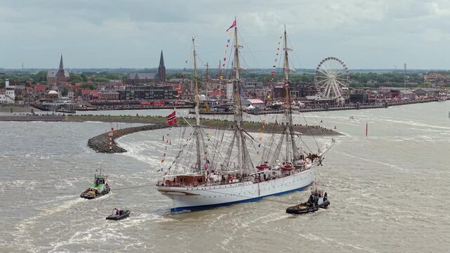 Large tall ship entering Harlingen harbor with escort boats