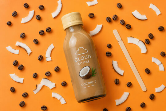 Coconut coffee bottle on a vibrant orange background with beans and coconut pieces. Perfect for beverage ads, packaging, banners, and social media.