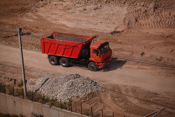 Red heavy dump truck driving on dirt road at construction site quarry during earthworks © Арман Амбарцумян