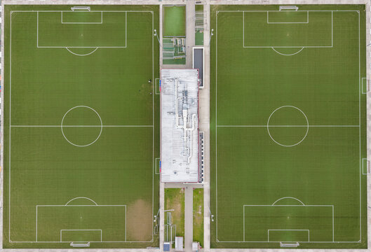 Aerial view of two green soccer fields separated by a central building complex in Diepenbeek, Belgium.