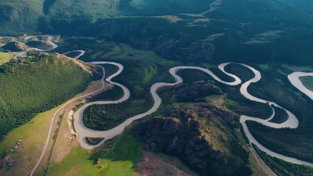 Aerial view of winding river meandering through Altai mountainous valley with forested slopes and rural road.