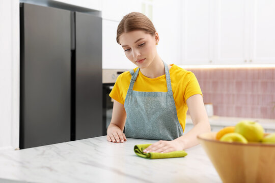 Teenage girl wiping island with rag in kitchen