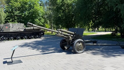 Obraz premium Military Memorial: A historical artillery piece stands as a monument in a park, with a military vehicle visible in the background, evoking remembrance of past conflicts.