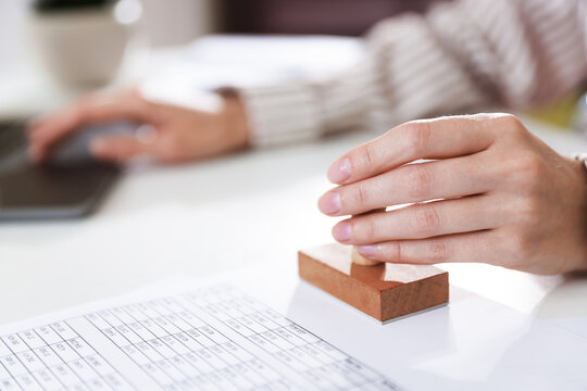 Woman stamping document while working with laptop at desk indoors, closeup. Space for text