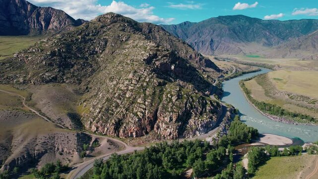 Aerial tracking shot river flowing around rocky hill in Altai mountain valley with gentle pan and tilt over winding bank landscape.