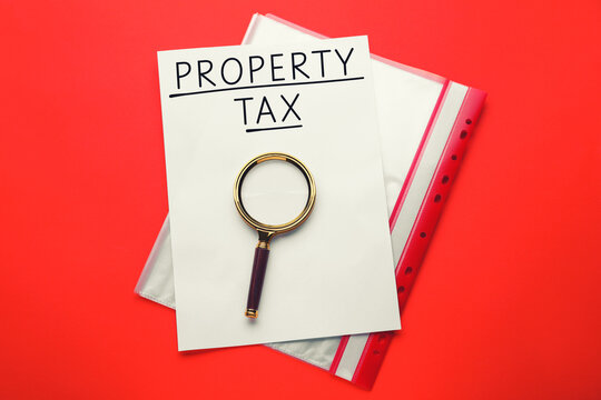 Property tax. Paper with words, magnifying glass and folder on red background, top view