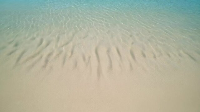 Aerial view of shallow, clear turquoise ocean water gently washing onto a sandy beach