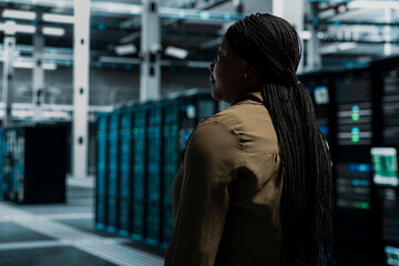 Fototapeta premium IT professional walking in server facility with mainframes supporting business needs. Data center staff member doing checkup, supporting electronics work at optimum performance for smooth operations.