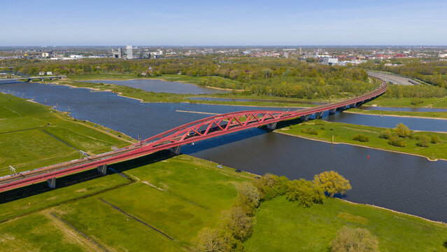 Aerial view of the Hanzeboog railway bridge spanning the IJssel river, surrounded by lush green meadows and the city skyline in Zwolle, Gelderland, Netherlands.