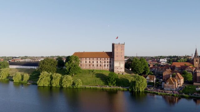 Aerial drone view of Koldinghus Castle in Kolding, Denmark on a summer evening with Danish flag, lake and old town