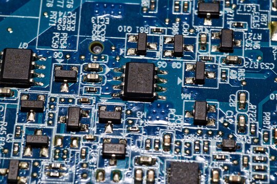 Macro shot of surface-mount components, integrated circuits, and microchips on a blue circuit board.
