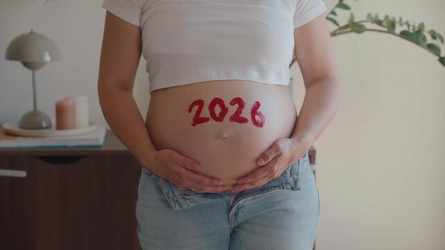 4K video of a pregnant woman with the red number 2026 painted on her bare belly, symbolizing her baby's due date year and the countdown to motherhood