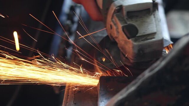 Close-up of a worker operating an electric angle grinder on a steel structure, producing a stream of bright sparks in a workshop