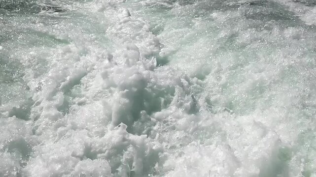 A close-up, slow-motion panning shot of a speedboat&rsquo;s wake along the coast, sweeping across foaming water, spray, and powerful, flowing wash.