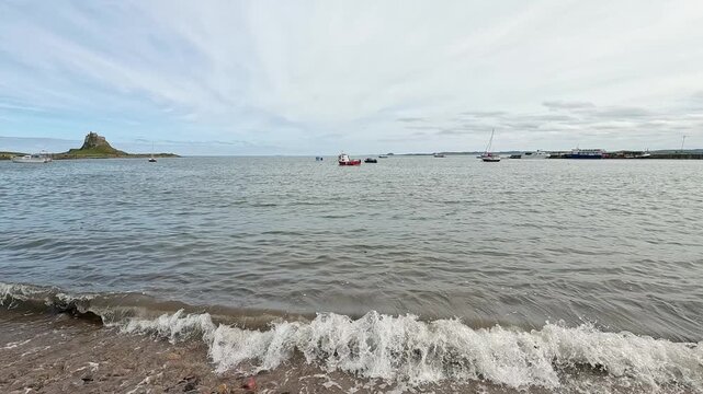 A slow-motion static shot of boats moored off Holy Island on the North East coast, gently floating on calm waters with soft coastal light and distant horizon.