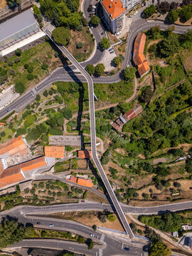 Aerial view of Carpinteira Pedestrian Bridge spanning the valley with surrounding greenery, winding roads, and terracotta-roofed buildings in Covilha, Castelo Branco District, Portugal.