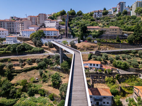 Aerial view of Carpinteira Pedestrian Bridge spanning the valley with modern architecture, surrounding terraced hills, and the cityscape of Covilha, Castelo Branco District, Portugal.