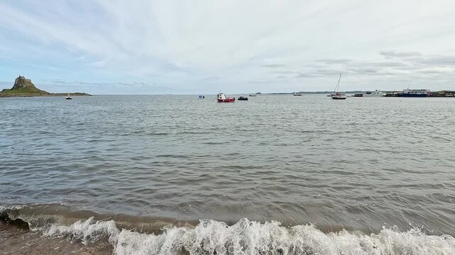 A slow-motion pull-back shot of boats moored off Holy Island on the North East coast, revealing calm waters, distant horizon and rugged coastal scenery.