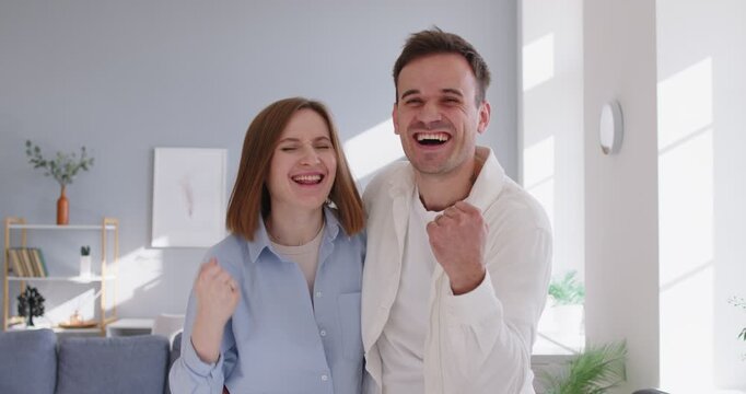 Happy excited couple celebrate success with a cheerful yes gesture. They stand in modern room at home, sharing joy and motivation after great news. Clear message of victory, success, and unity.