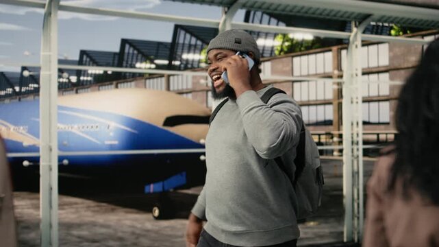 Relaxed man walking in airport terminal uses smartphone to call friends, having fun, happy African American tourist enjoying mobile phone discussion, doing vacation air travel to foreign country.