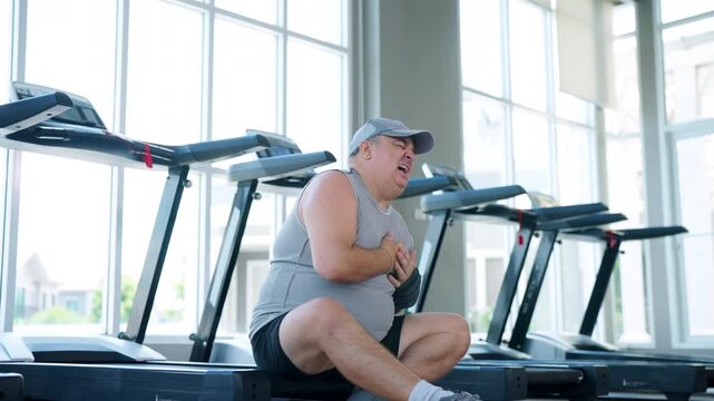Mature overweight man suffering chest pain after intense workout at fitness gym. Exercise risk heart health medical emergency overtraining fatigue healthy aging and fitness awareness