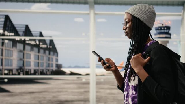 Woman holds phone inside modern airport terminal, doing online check-in, while girl uses smartphone to access internet airline website and check plane timetable.