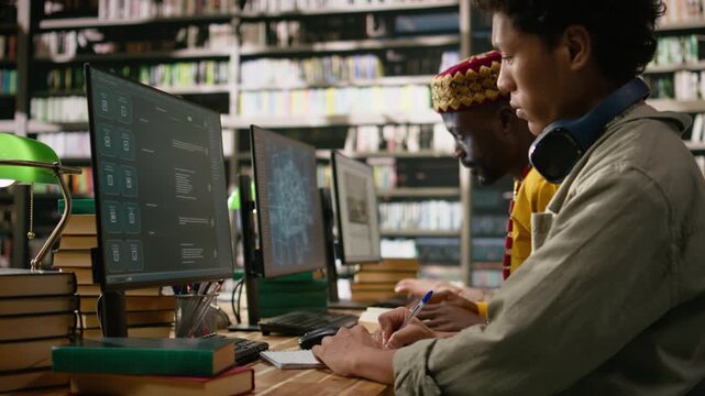 Asian young learner writing notes near chatbot on monitor screen at library desk beside AI interface, desktop shows virtual assistant automation, digital learning computer class, for coursework.