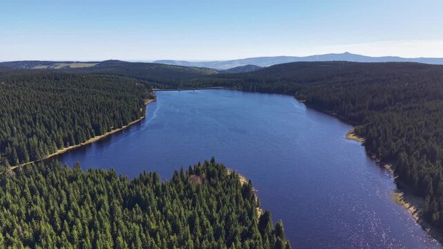 Clear horizon reservoir aerial study over mature forest, calm reflective water and mountain silhouette, high