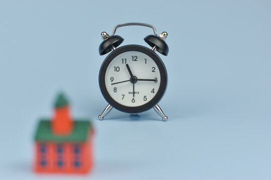 Hand holds alarm clock above tiny house