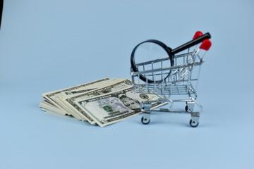 Shopping cart holds magnifying glass above stacked bills © Nazir