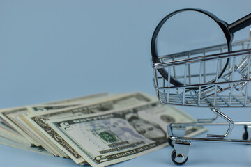 Shopping cart holds magnifying glass above stacked bills © Nazir
