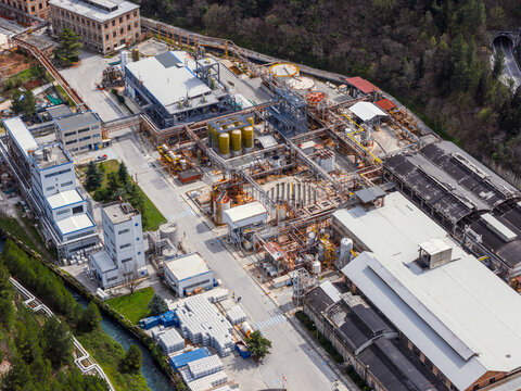 Aerial view of the Edison industrial plant featuring complex piping systems, storage tanks, and factory buildings surrounded by lush greenery in Bussi Officine, Abruzzo, Italy.