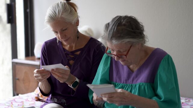 A mature daughter visits her elderly mother at a senior care facility. They share stories and look at photos together.