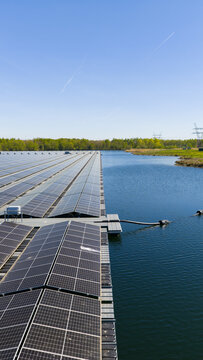 Aerial view of a floating solar farm with rows of photovoltaic panels installed on a lake, surrounded by green trees and clear blue sky in Zwolle, Overijssel, Netherlands.