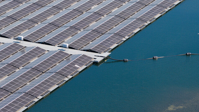 Aerial view of a large floating solar farm with rows of photovoltaic panels installed on a platform over calm blue water in Zwolle, Overijssel, Netherlands.
