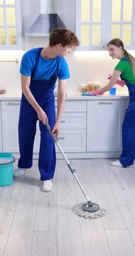 Teenage workers cleaning kitchen and mopping floor indoors. Part-time job