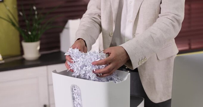 Man taking out cut paper pieces from shredder bin in office, closeup
