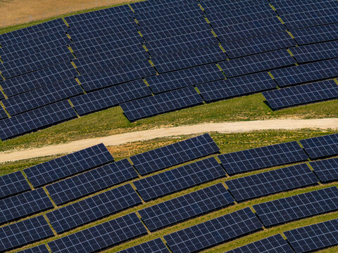 Aerial view of solar panels arranged in rows across a grassy field with a dirt path in Jacionys, Vilnius County, Lithuania.