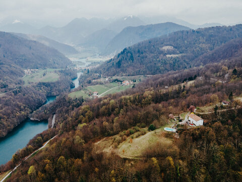 Aerial view of the Soca River winding through forested hills and mountains near a house with a swimming pool, Most na Soci, Tolmin, Slovenia.