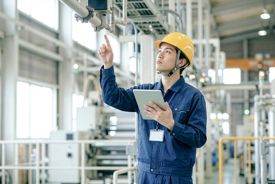 タブレットを使って工場設備を点検するヘルメットを着用した日本人若手男性エンジニア