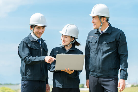 A male and female construction worker in work clothes are having a meeting at a construction site, looking at their laptops.