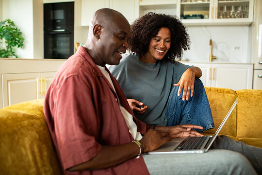 Two people using a laptop on a sofa at home