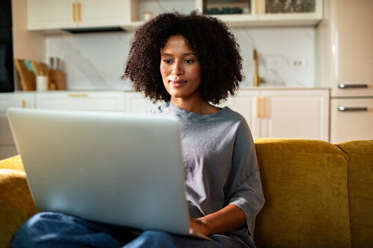 Woman working on laptop on sofa in home kitchen