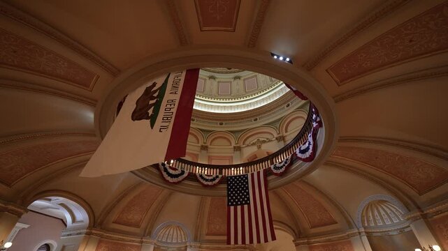 Camera looks upwards at the rotunda dome inside the California State Capitol in Sacramento showing flags and architectural features